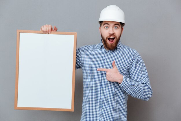 Shocked happy bearded builder holding blank board