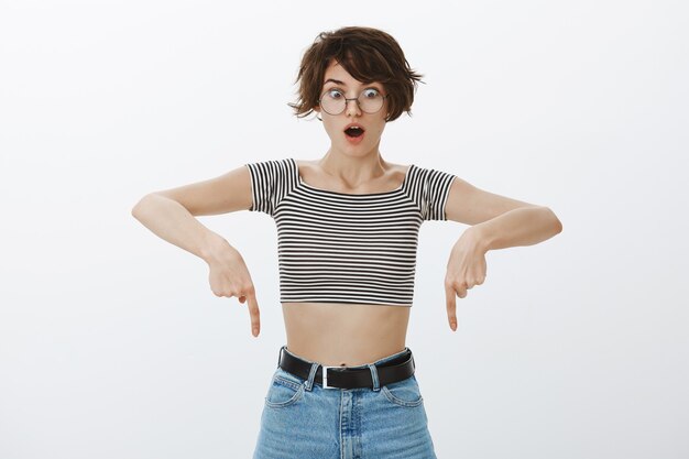 Shocked hipster girl in cropped top pointing fingers down