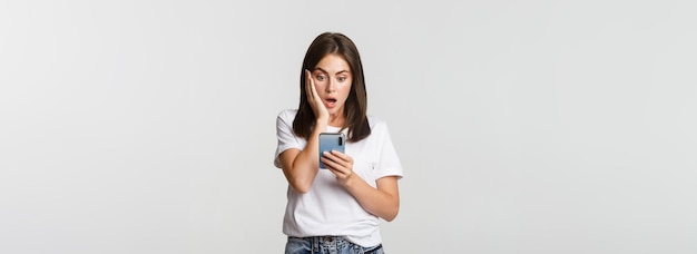 Shocked and impressed brunette girl looking amazed at smartphone screen