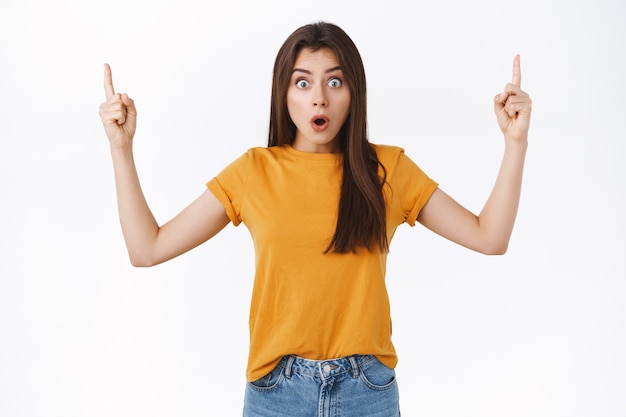 Shocked, impressed and speechless pretty caucasian woman, gasping widen eyes as stare camera stunned, pointing raised fingers up, express surprise check out amazing event, white background