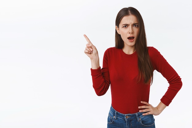 Shocked and insulted bothered upset caucasian girl in red sweater complaining on offensive promo gasping shook frowning frustrated as pointing upper left corner with aversion