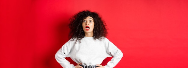 Free photo shocked italian woman with curly hair gasping and staring at camera astonished open mouth standing i