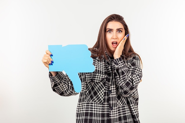 親指ダウンサインを保持し、白い背景の上に立つショックを受けた女性