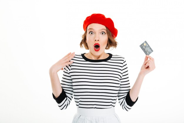 Shocked lady with opened mouth holding credit card and looking camera isolated