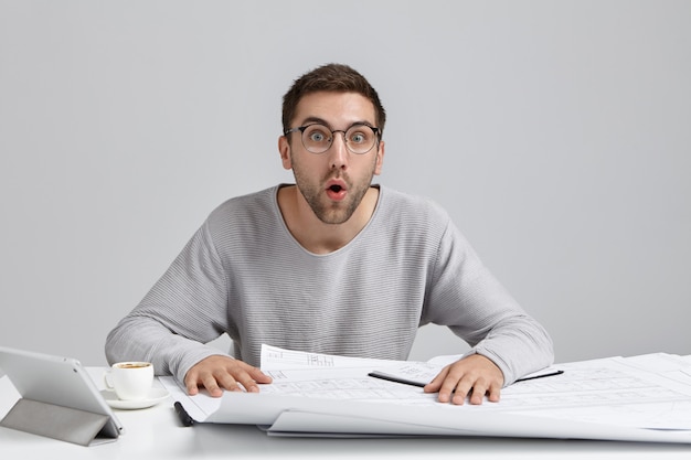 Shocked male engineer develops new image design, looks with opened mouth as remembers about important meeting