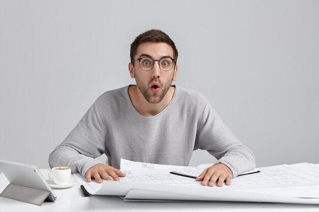 Shocked male engineer develops new image design, looks with opened mouth as remembers about important meeting