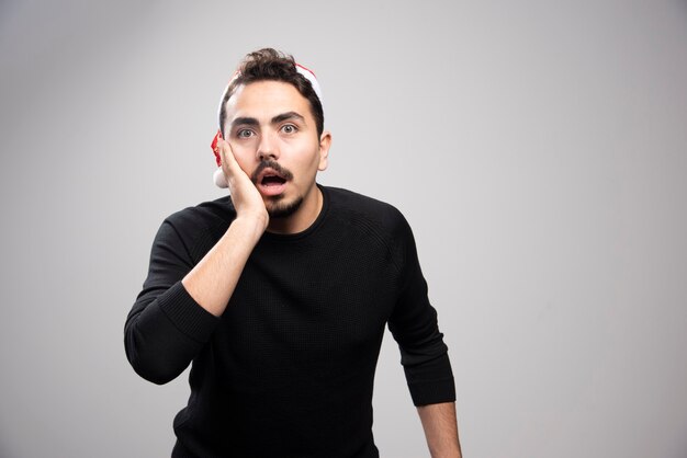 Uomo scioccato in maglione nero che indossa il cappello di babbo natale.