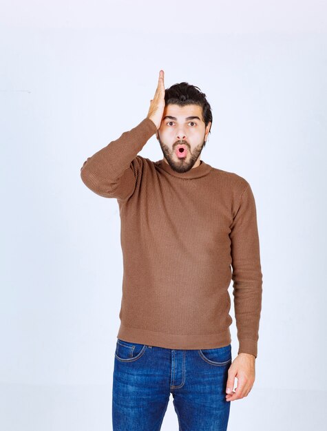 A shocked man model standing and holding his head over white wall. High quality photo