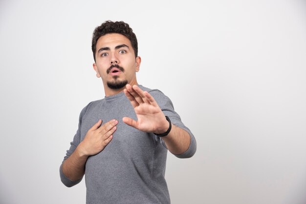 A shocked man posing with hands on a white wall.