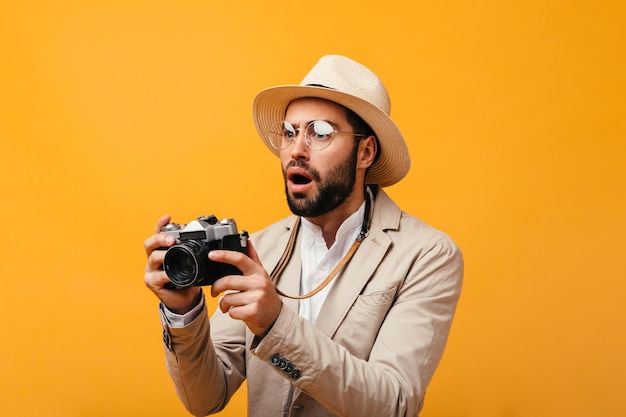 Шокированный мужчина в стильном наряде позирует с ретро-камерой