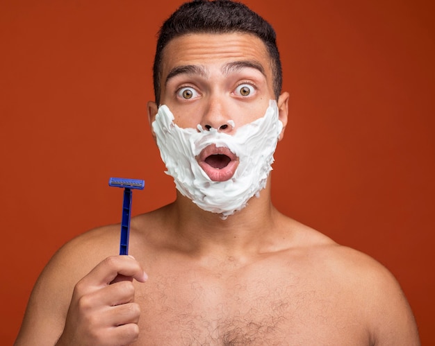 Foto gratuita uomo scioccato con schiuma da barba sul viso che tiene il rasoio