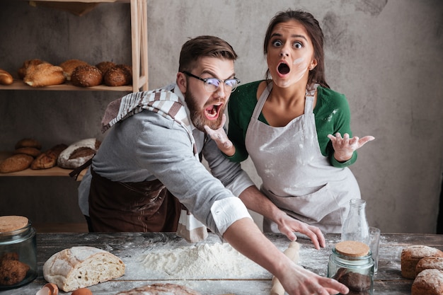 Shocked man and woman standing near table with flour