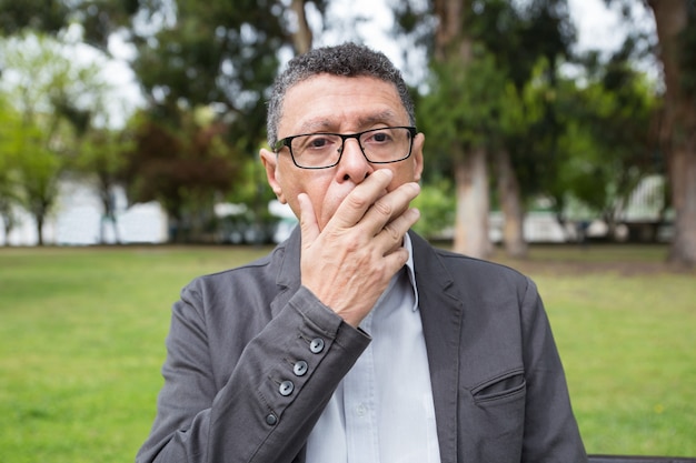 Shocked middle-aged man covering mouth with hand in park