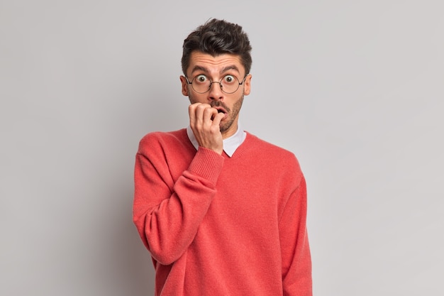 Free photo shocked nervous man bites finger nails stares through optical glasses