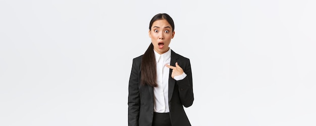 Free photo shocked and offended young asian woman in suit pointing at herself with astounded panic face being accused businesswoman looking insulted after being named white background