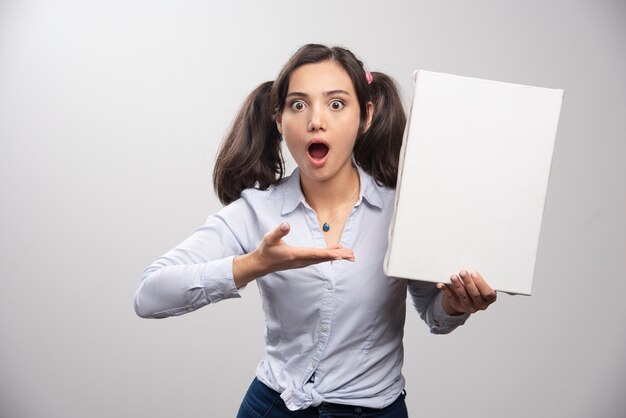 Shocked painter pointing at empty canvas on gray wall. 