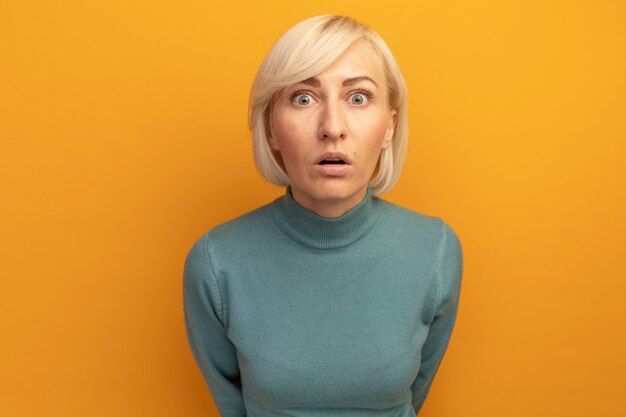 Shocked pretty blonde slavic woman looks at front isolated on orange wall