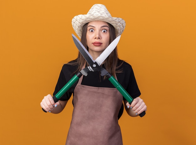 Shocked pretty caucasian female gardener wearing gardening hat holding gardening scissors