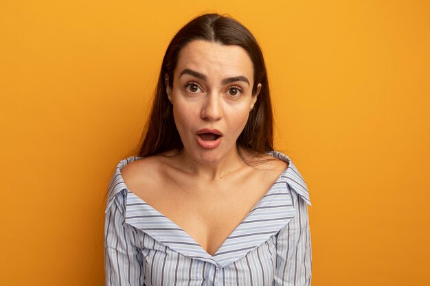 Shocked pretty woman looks at front isolated on orange wall