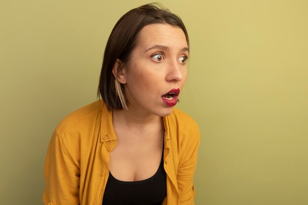 Shocked pretty woman looks at side isolated on olive green wall