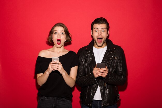 Shocked punk couple holding their smartphones while looking