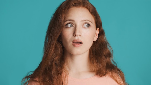 Shocked redhead girl with open mouth amazedly looking away over colorful background