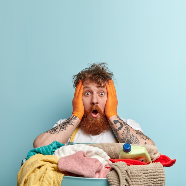 Free photo shocked redhead housekeeper faces troublesome situation, keeps both hands on face, has eyes popped out, messy hair