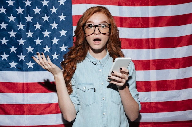 Shocked redhead young lady standing over USA flag