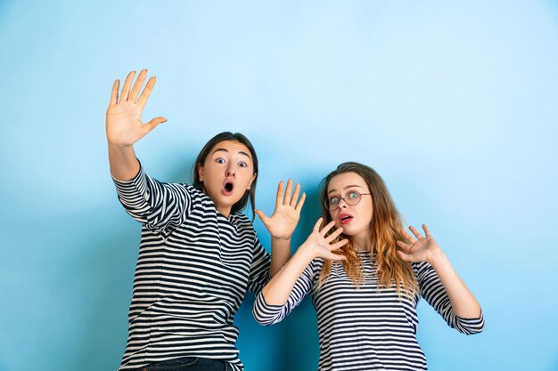 Шокированные и напуганные молодые эмоциональные женщины изолированы на градиентной синей стене студии