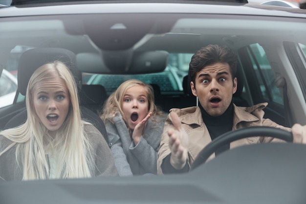 Free photo shocked scared young man sitting in car with family