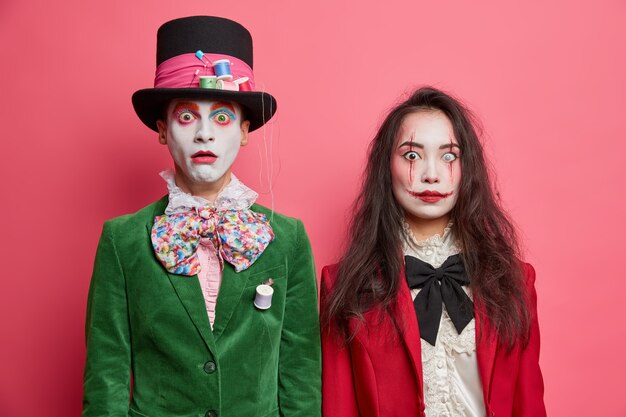 shocked scary couple celebrate halloween have professional makeup and wear costumes pose next to each other against pink wall