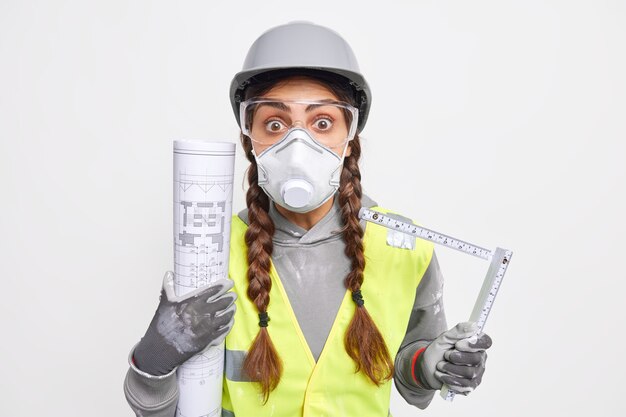 Shocked skilled female engineer holds blueprint and tape measure works on new construction project