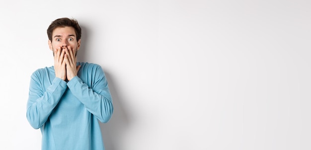 Free photo shocked and startled cauacasian man gasping and covering mouth with hands staring at something scary