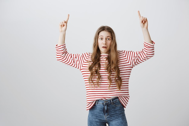 Free photo shocked and startled girl looking worried and pointing fingers up