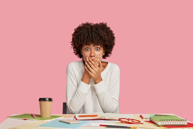 Shocked student girl posing at the desk against the pink wall