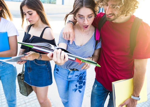 Shocked students reading textbook near friends