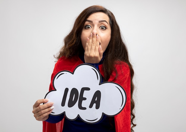 Free photo shocked superwoman with red cape puts hand on mouth and holds idea bubble isolated on white wall