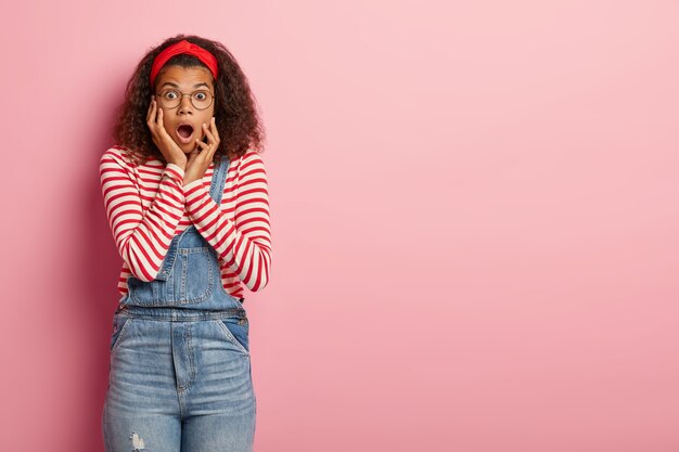 Shocked teenage girl posing in overalls with curly hair