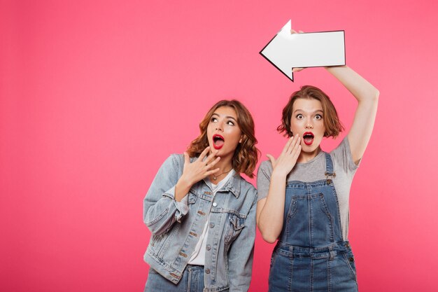 Shocked two ladies friends holding arrow.