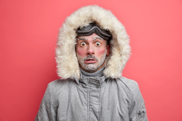 Shocked unshaven man wears warm jacket with hood perfect for frosty winter days has face covered with snow being not adapted to severe cold conditions has active rest.