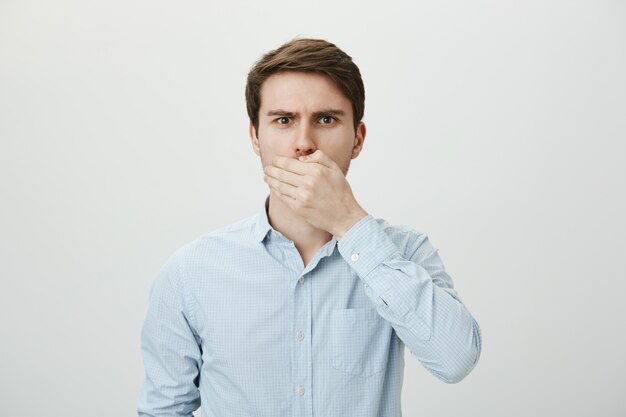 Shocked upset brunette man shut mouth with hand