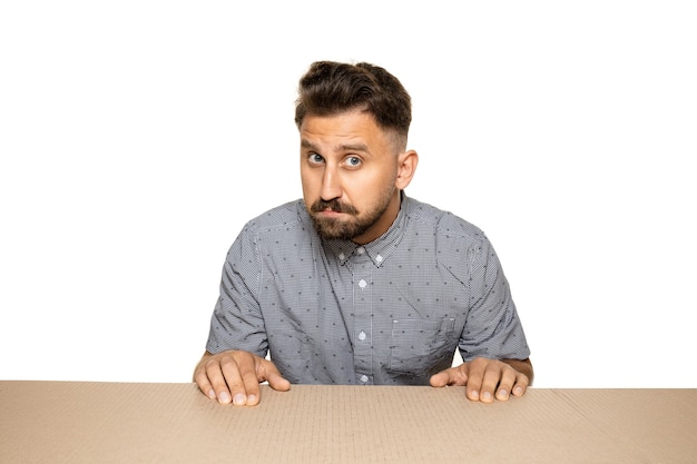 Shocked and upset man opening the biggest postal package. Sad and disappointed young male model on top of cardboard box