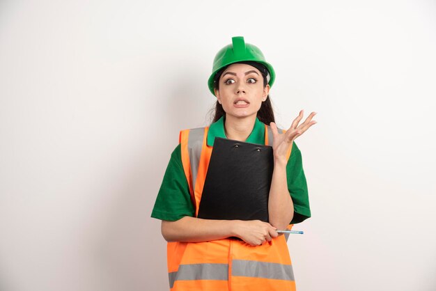 Shocked woman constructor wearing green helmet standing with clipboard . High quality photo