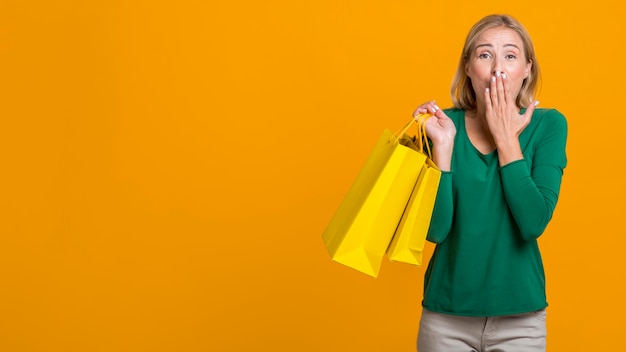 Shocked woman covering her mouth while holding many shopping bags with copy space