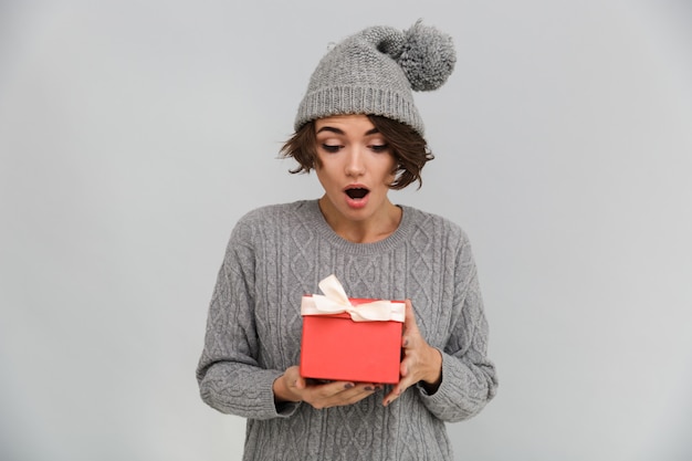 無料写真 セーターと贈り物を持って暖かい帽子に身を包んだショックを受けた女性。