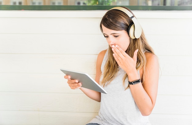 Shocked woman in headphones using tablet on street