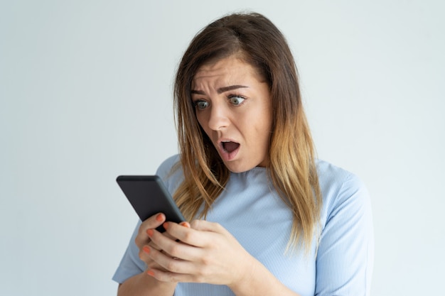 Shocked woman holding smartphone and looking at its screen. Lady reading message.