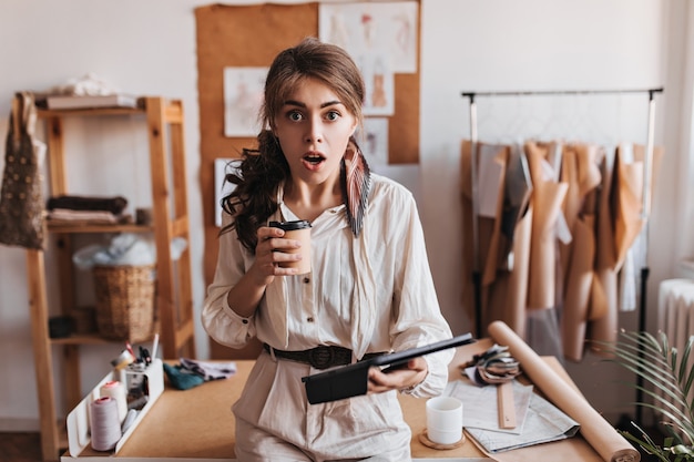 Shocked woman holds coffee cup and computer tablet