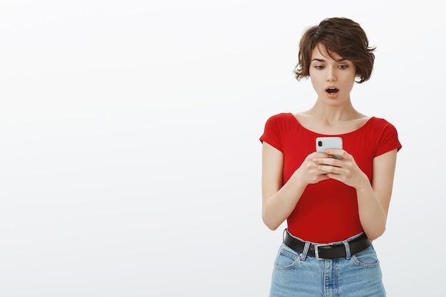 shocked woman look at mobile phone with dropped jaw, stare at smartphone in awe