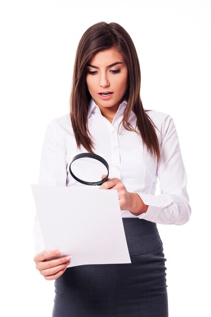 Shocked woman looking through a magnifying glass on documents